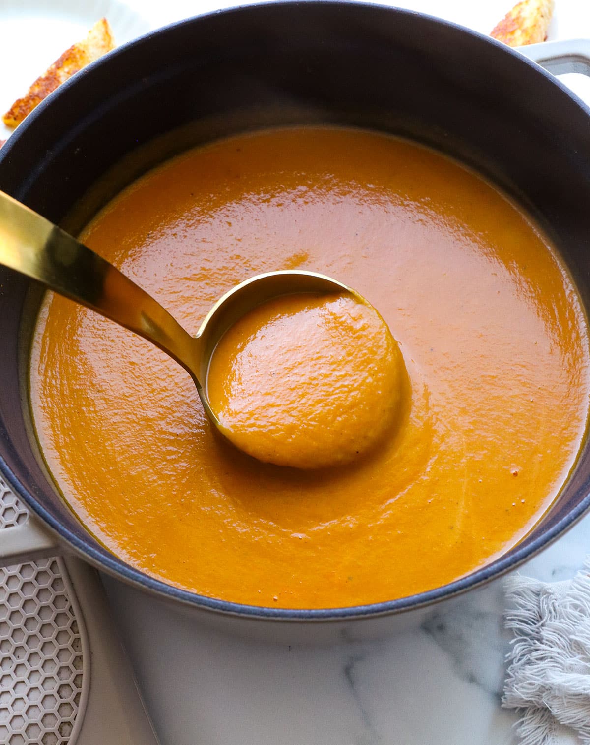 gold ladle dipped into the pot of pumpkin tomato soup to show the final texture.