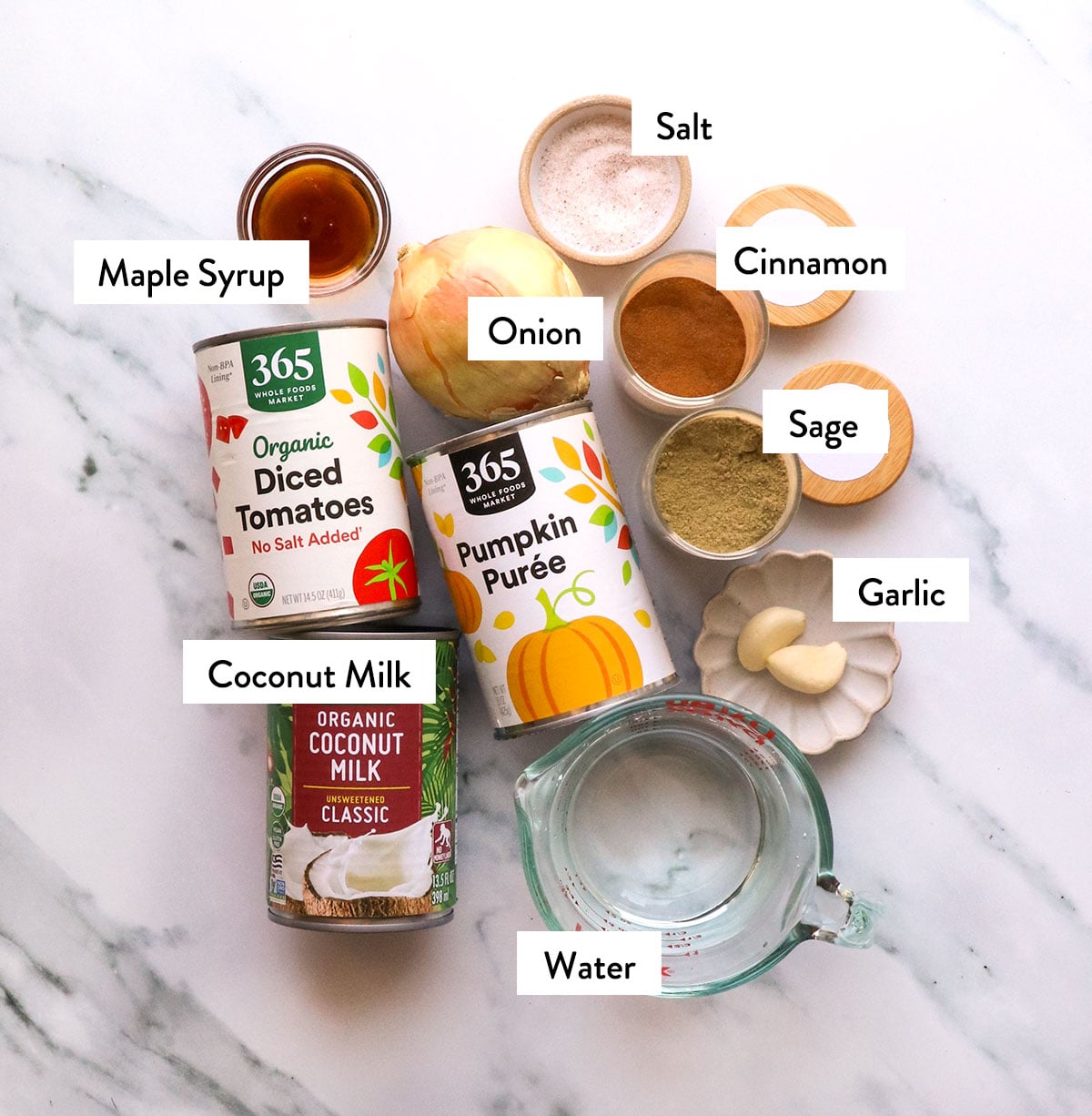 cans of diced tomatoes, pumpkin puree, and coconut milk next to an onion and jars of spices.