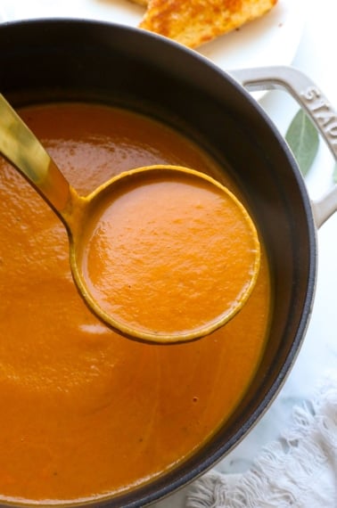 pumpkin tomato soup lifted up on a ladle.