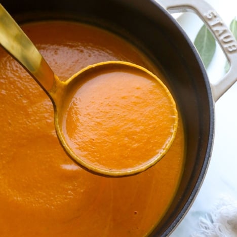 pumpkin tomato soup lifted up on a ladle.