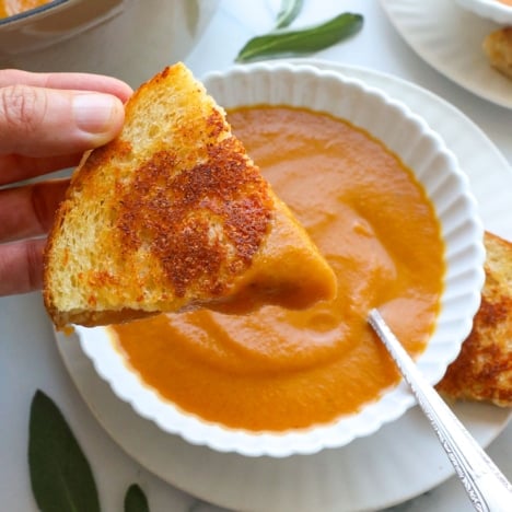grilled cheese wedge dipped into pumpkin tomato soup and lifted with a hand.