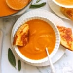 pumpkin tomato soup served in a white bowl with a grilled cheese wedge.