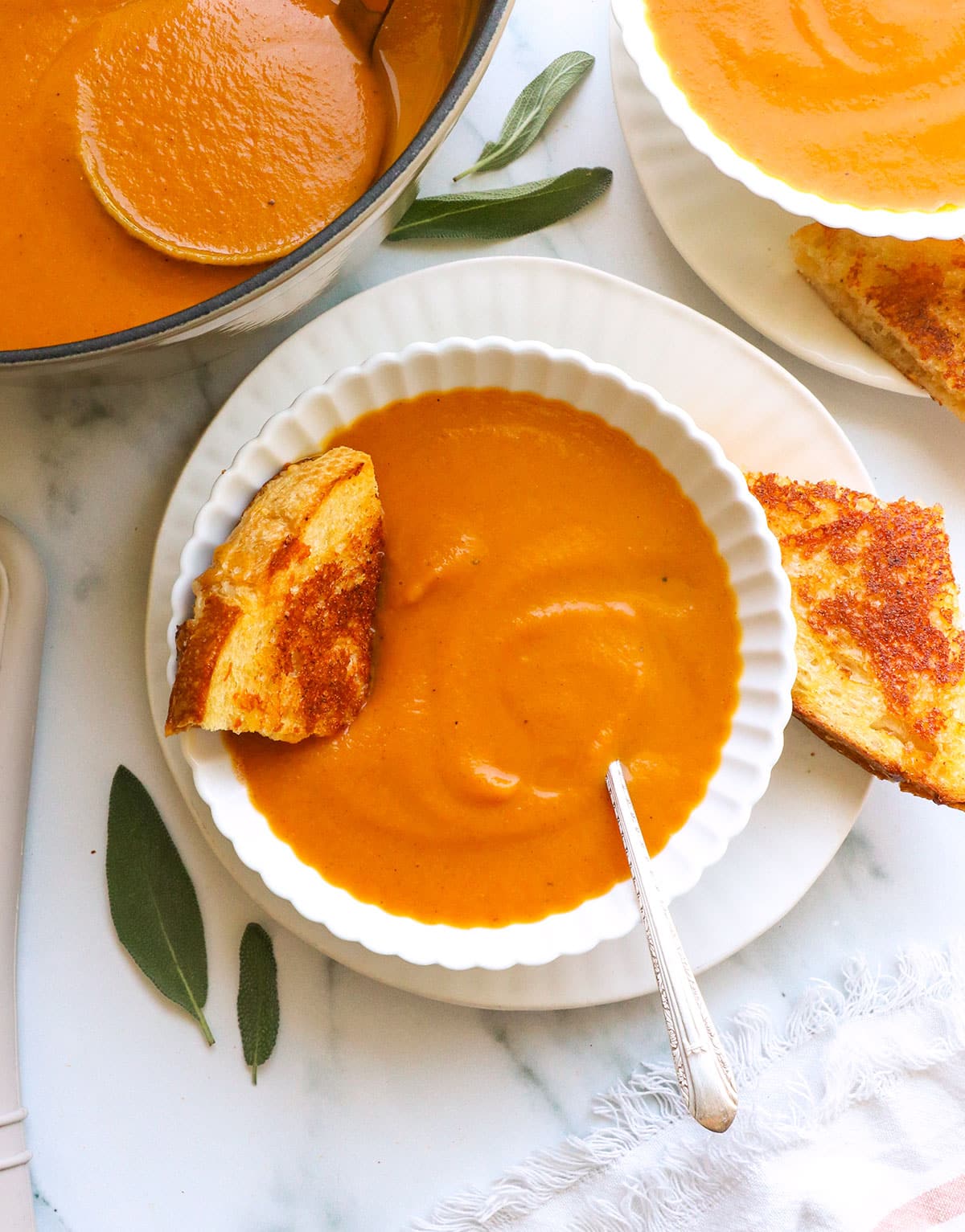 pumpkin tomato soup served in a white bowl with a grilled cheese wedge.