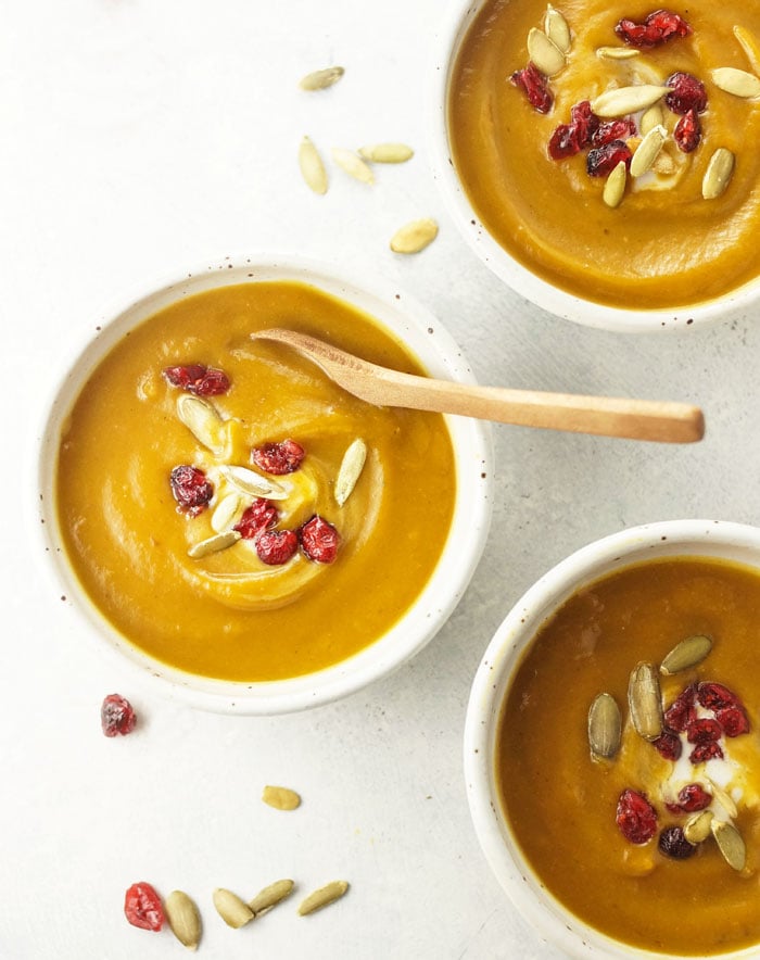 bowl of curried butternut squash soup with pumpkin seeds and dried cranberries on top