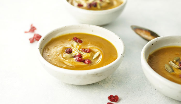 bowl of curried butternut squash soup with pumpkin seeds and dried cranberries on top