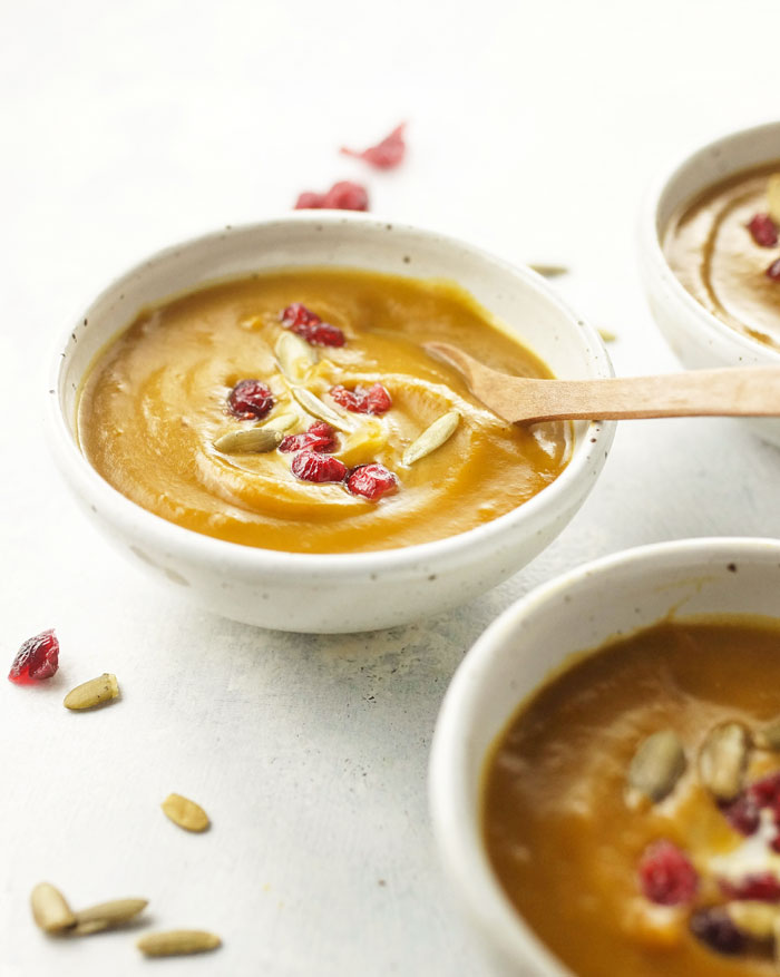 bowl of curried butternut squash soup with dried cranberries and pumpkin seeds on top