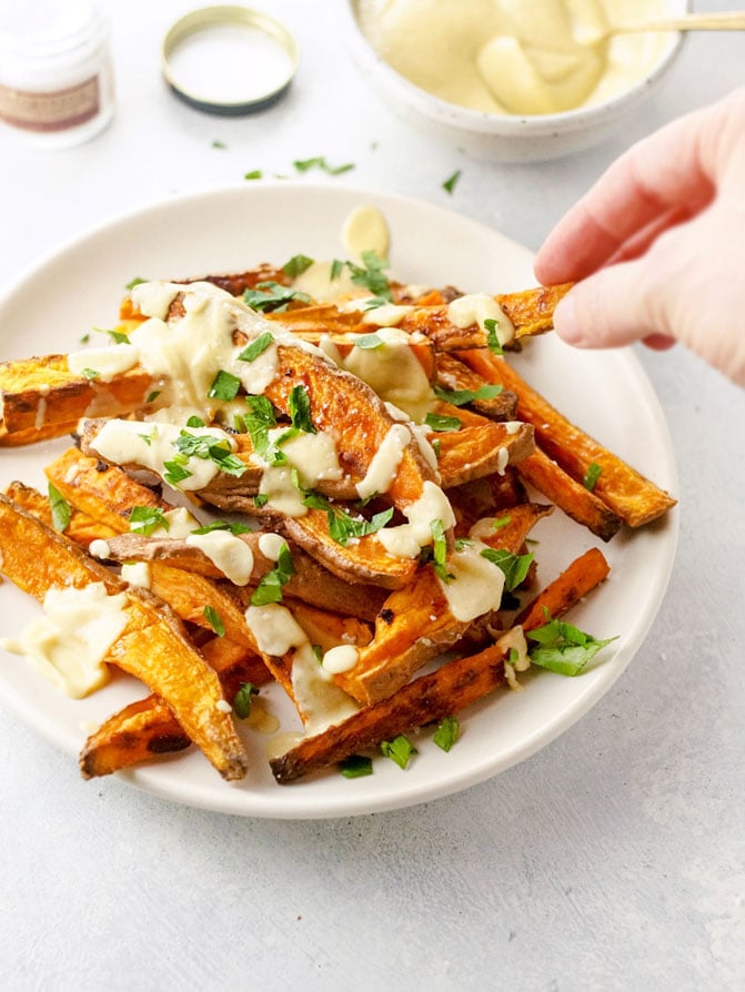sweet potato fries with roasted cauliflower cheese sauce and green onion slices on top 
