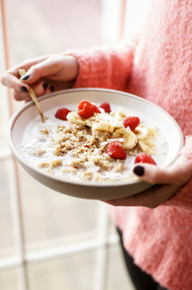 overhead quinoa breakfast bowl with raspberries held by woman