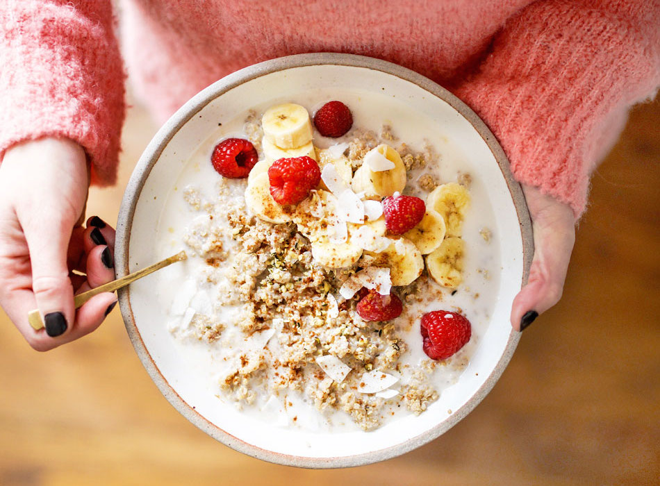 holding a bowl of quinoa breakfast with raspberries and bananas on top