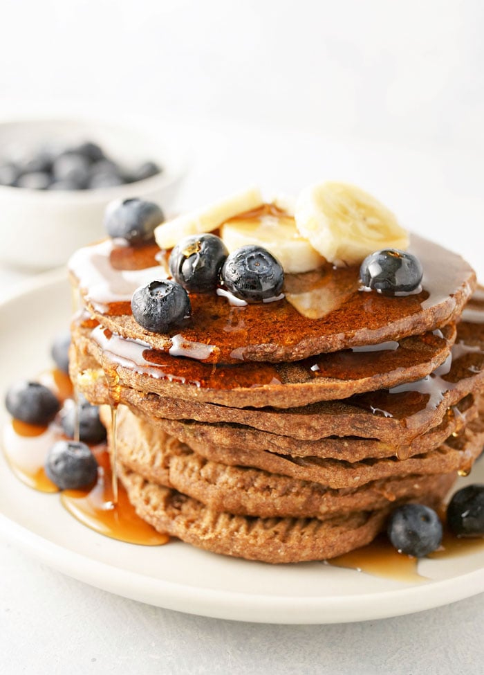 stack of baked buckwheat banana pancakes with blueberries, bananas, and syrup on top