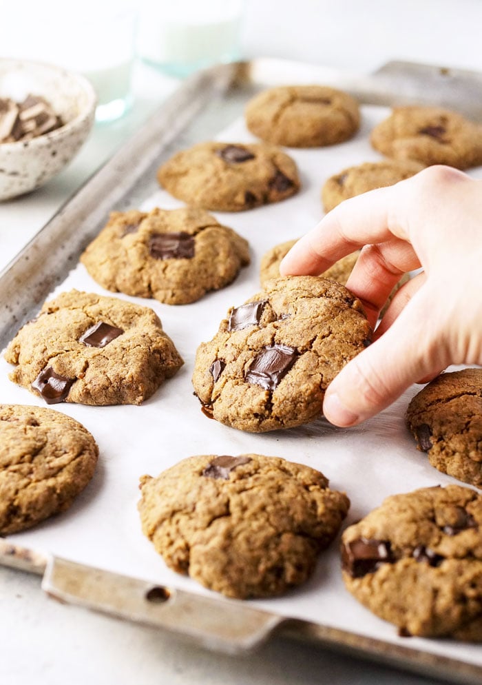 hand picking up a buckwheat chocolate chip cookie from a pan