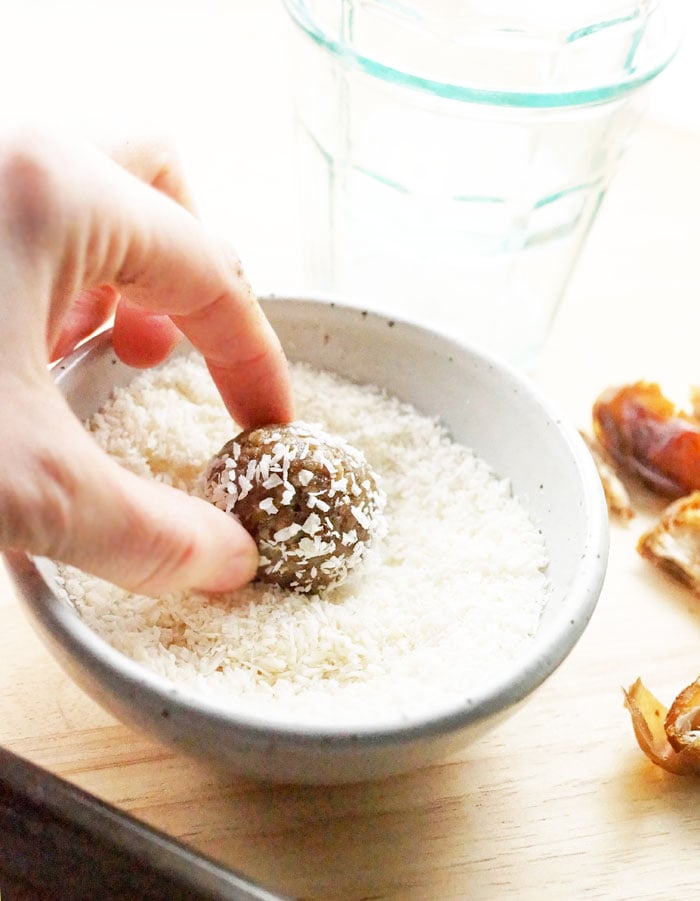 3-Ingredient Nut-Free Energy Bites being dipped in a bowl of coconut flakes