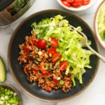 quinoa burrito bowls in a black bowl with shredded lettuce and tomatoes.