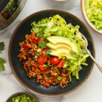 Instant pot quinoa burrito bowls with lettuce tomatoes and avocado slices on top.