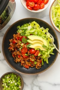 Instant pot quinoa burrito bowls with lettuce tomatoes and avocado slices on top.