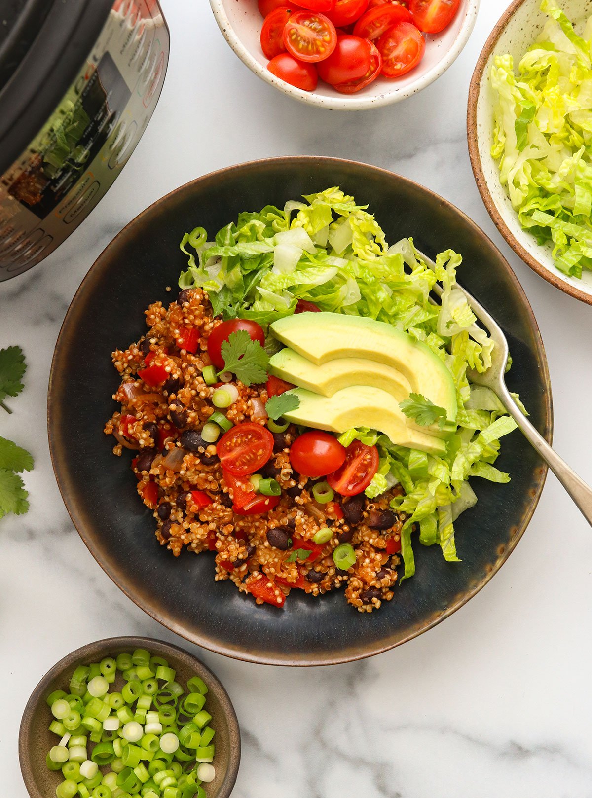 Instant pot quinoa burrito bowls with lettuce tomatoes and avocado slices on top.