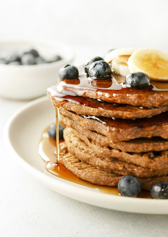 baked buckwheat pancakes stacked on a plate with blueberries, bananas, and syrup on top