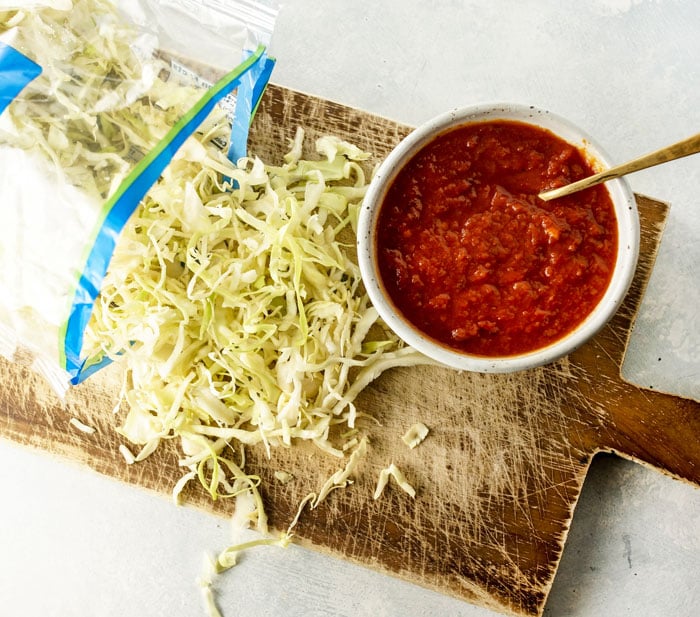 shredded cabbage and bowl marinara sauce on a cutting board