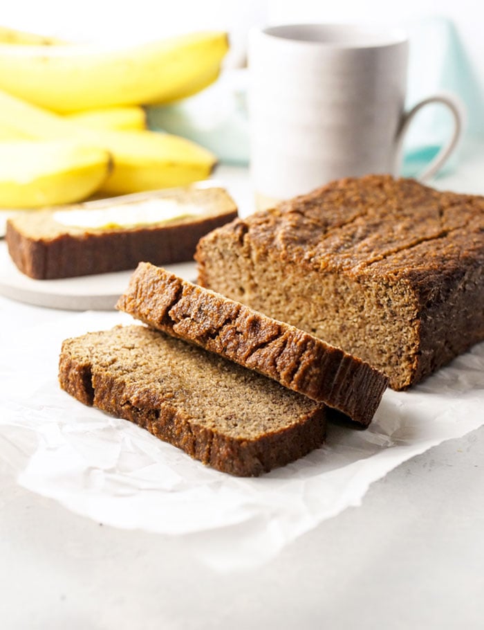 coconut flour banana bread loaf sliced with bananas and a coffee mug behind it