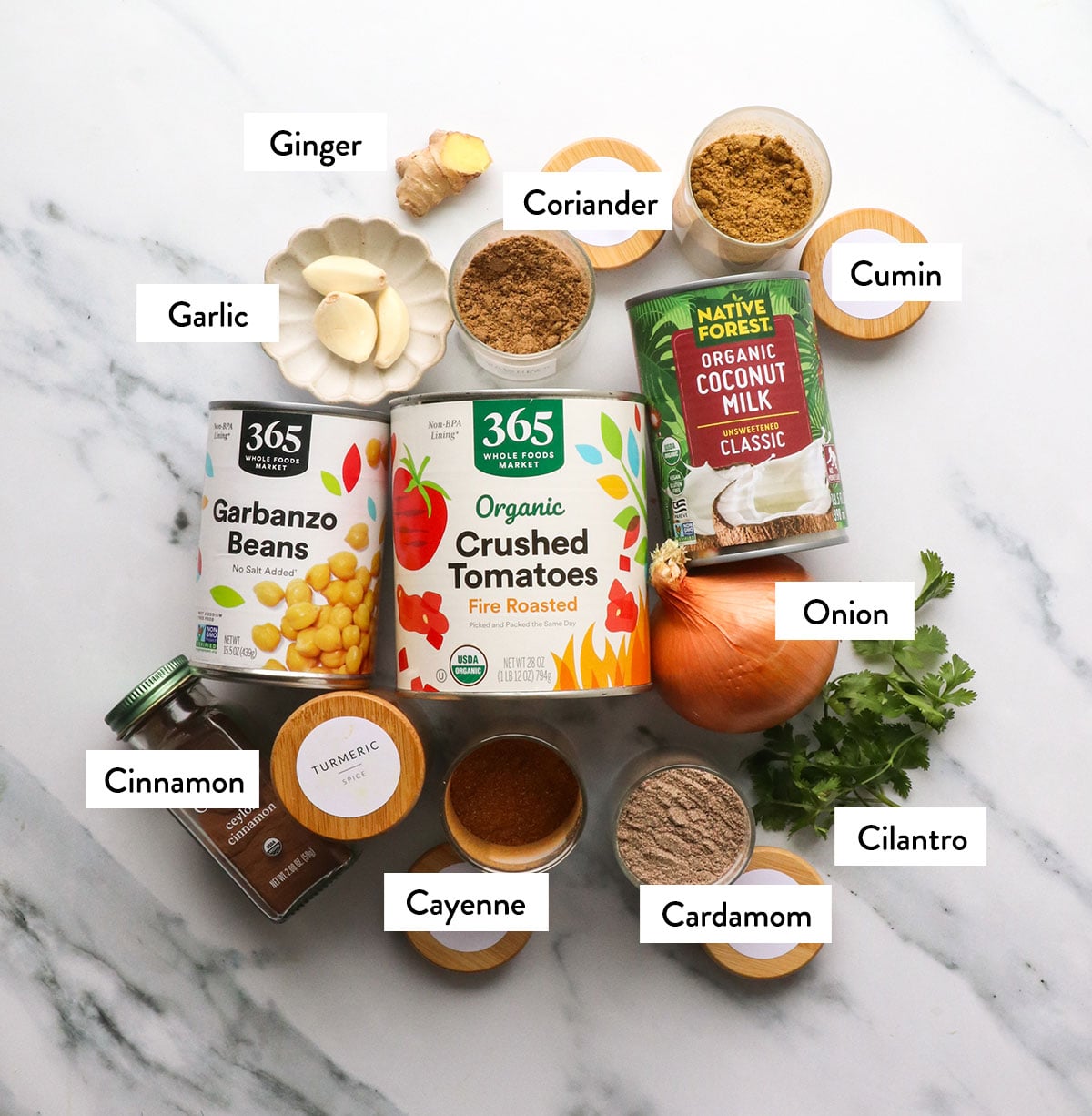 chickpeas, crushed tomatoes, coconut ilk, and spices labeled on a white surface. 