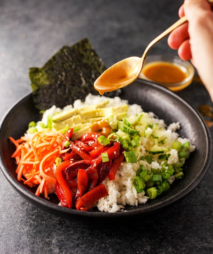 pouring soy-ginger dressing with a spoon over sushi bowl