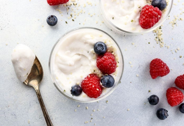 a spoonful of coconut milk yogurt, next to a cup of coconut milk yogurt topped with berries