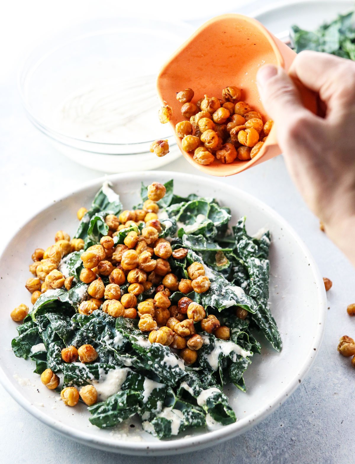 pouring roasted chickpeas over kale salad