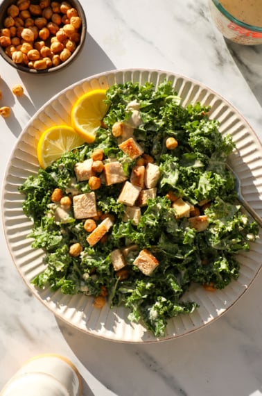 kale caesar salad topped with chicken and tahini dressing.