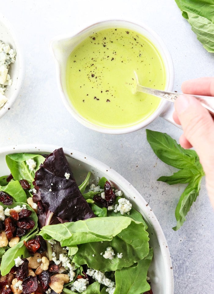 hand stirring a bowl of orange basil vinaigrette 