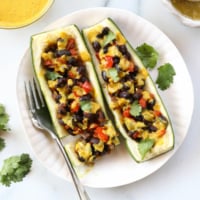 vegan stuffed zucchini boats on a white plate with a fork.