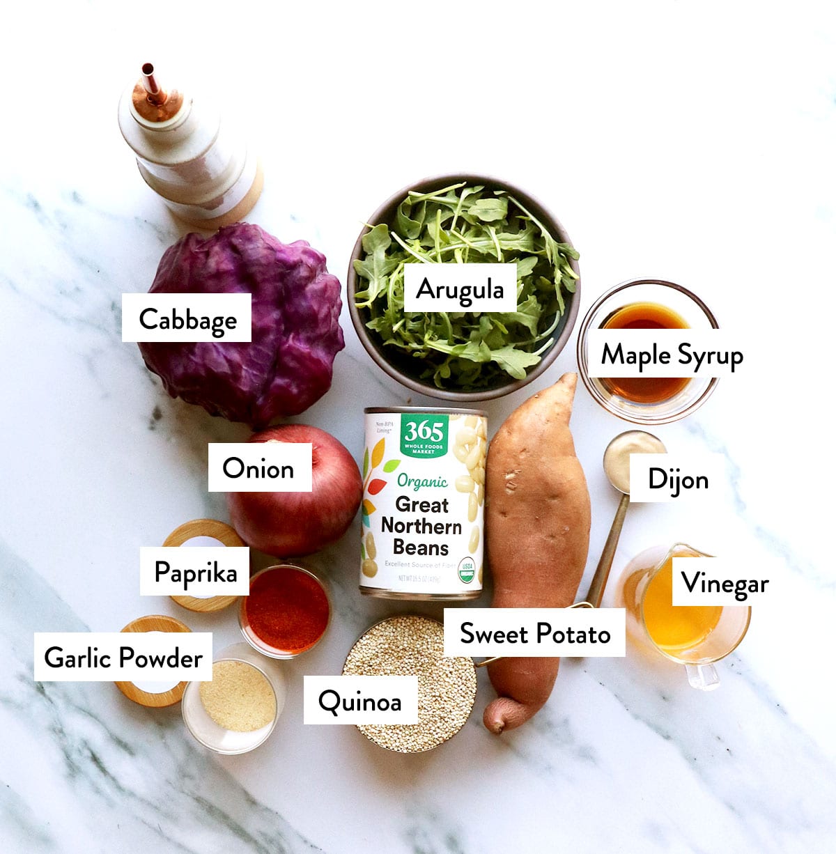 cabbage, arugula, white beans, quinoa, sweet potato, and onion on a white surface. 