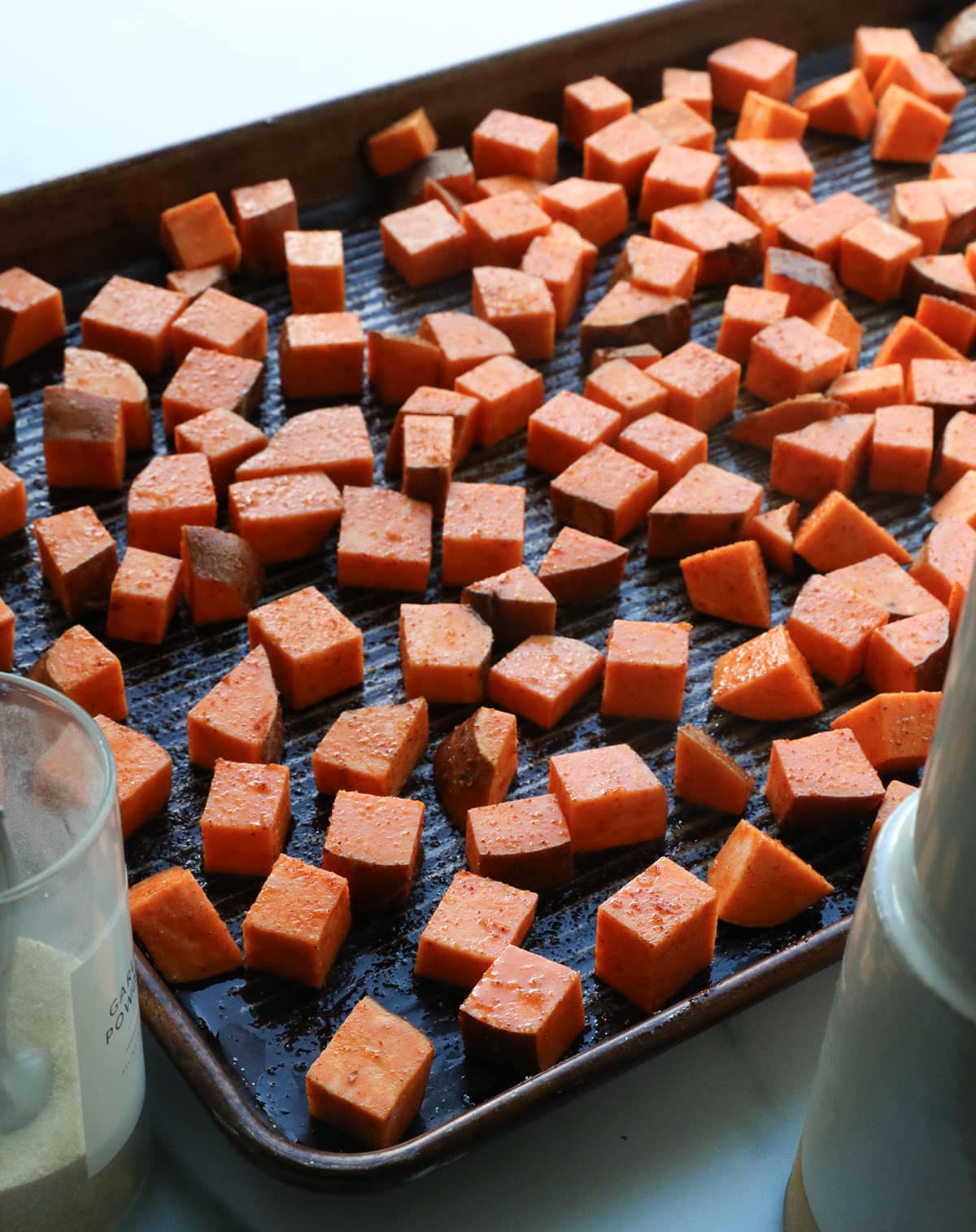 sweet potato cubes spread out on a rimmed baking sheet to bake. 