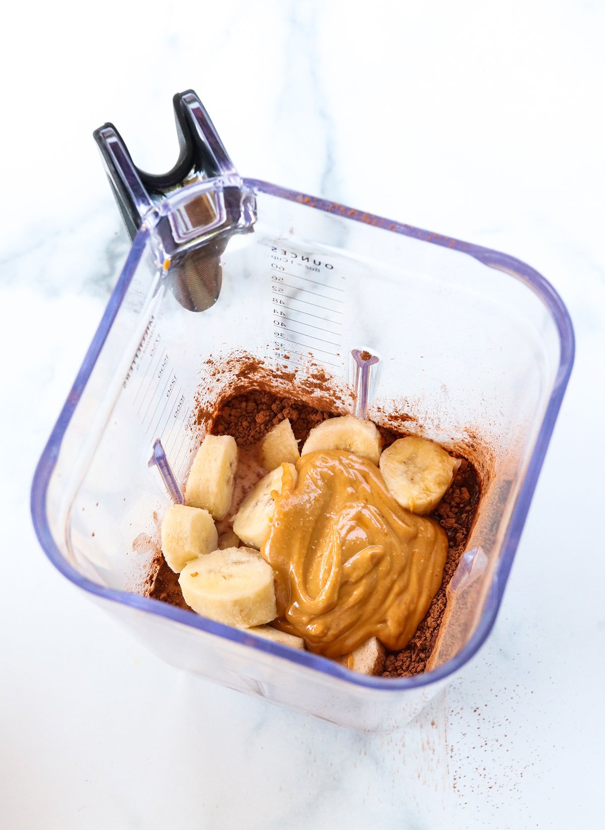 peanut butter, cocoa powder, and frozen bananas in a blender pitcher.
