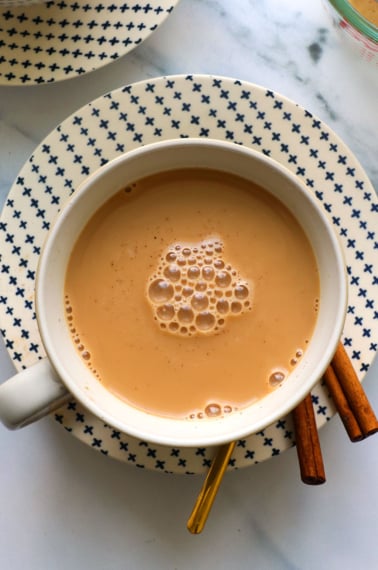 homemade chai latte in a mug with cinnamon sticks on a plate.