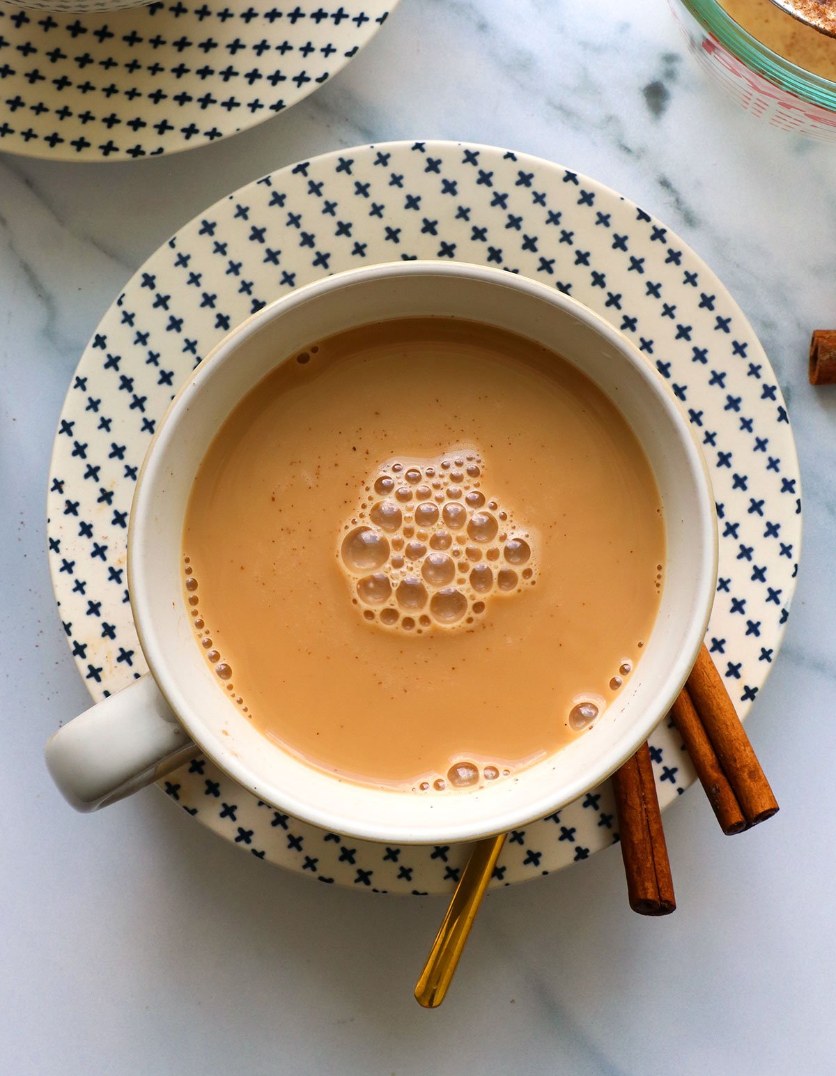 Homemade chai latte in cup with cinnamon sticks on plate.
