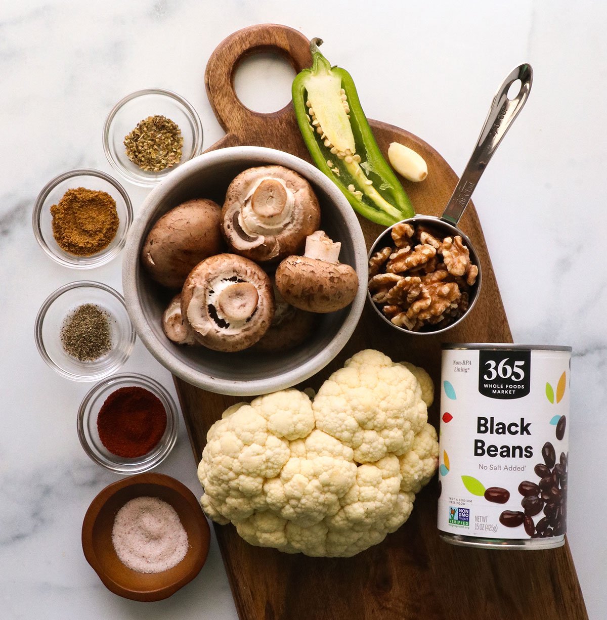 cauliflower, mushrooms, walnuts, black beans, and seasonings on a board.