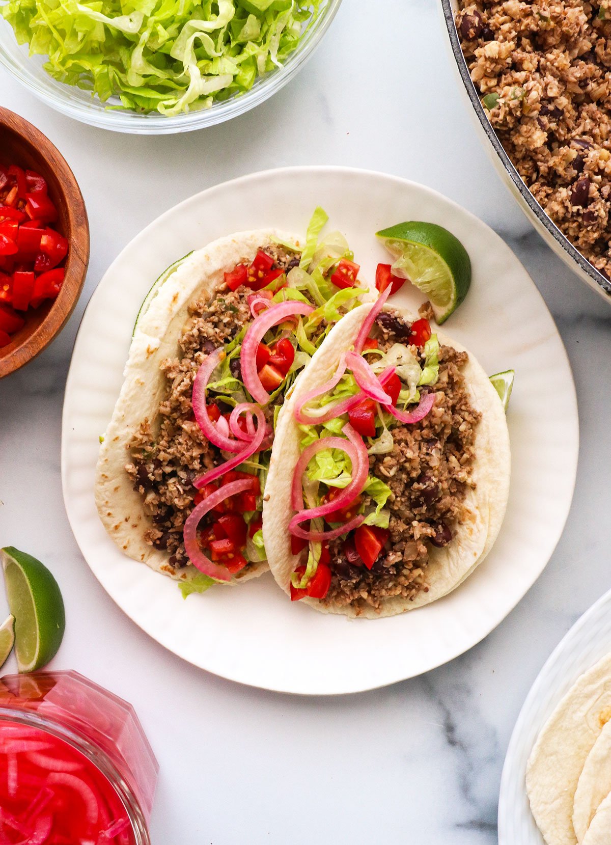 two vegan tacos served in tortillas with lime wedges and red onions.