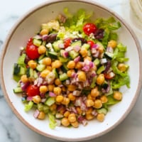 Mediterranean salad topped with chickpeas in a large white bowl.