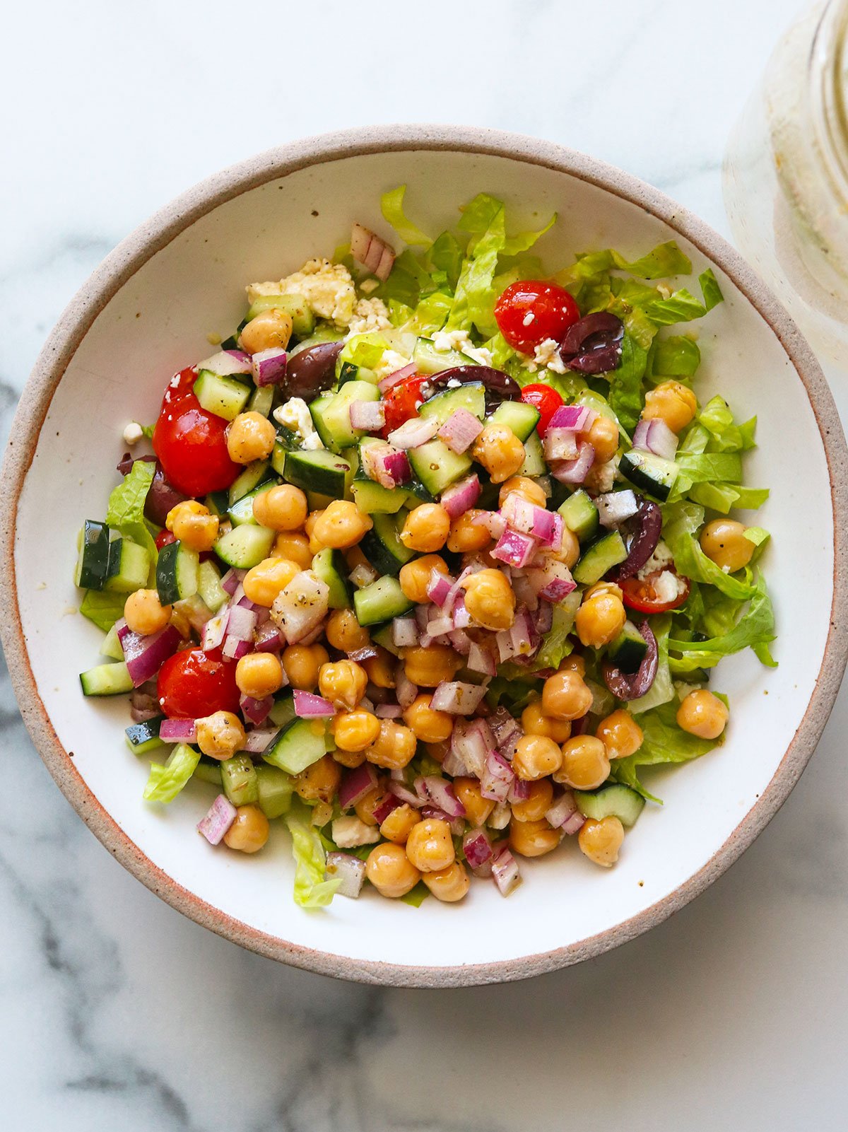Mediterranean salad topped with chickpeas in a large white bowl.