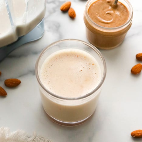 A glass of almond milk sitting next to a jar of almond butter.