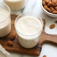 homemade almond milk on a cutting board with almonds on the counter.