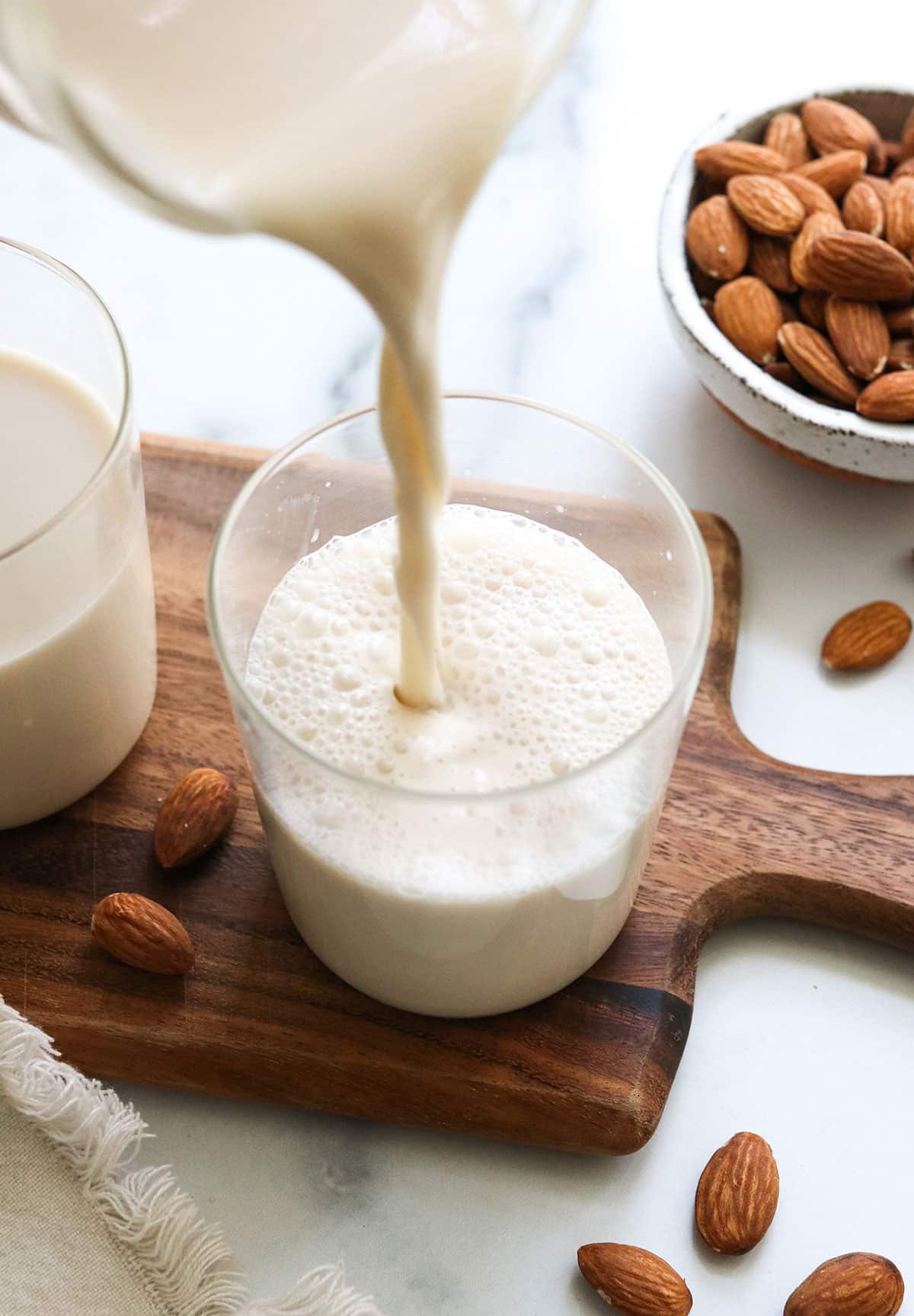 almond milk poured into a glass with almonds around it. 