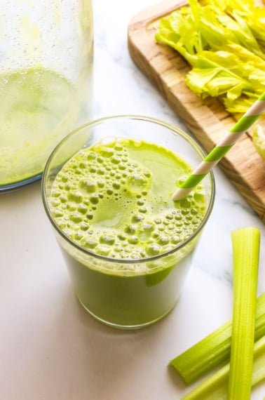 celery juice in a glass with a green striped straw.