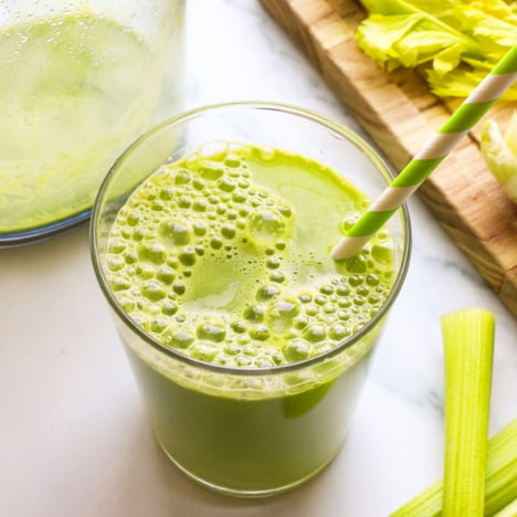 celery juice in a glass with a green striped straw.