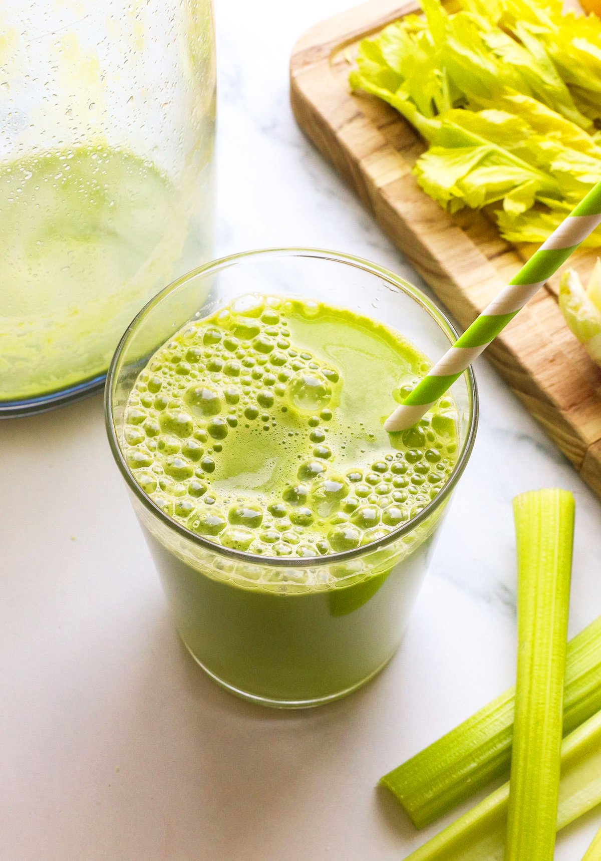 celery juice in a glass with a green striped straw.