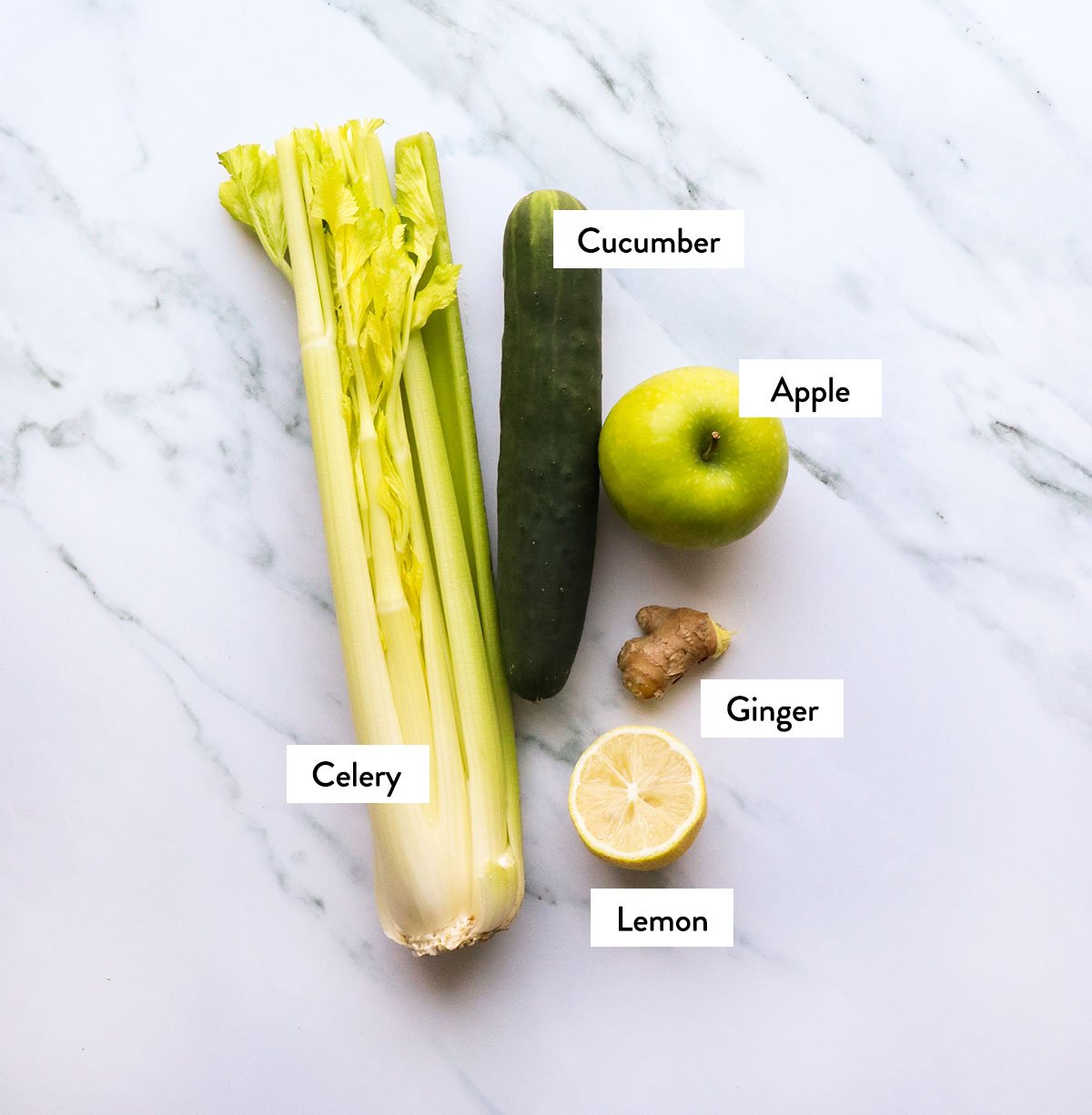 celery, green apple, cucumber, lemon and ginger labeled on a white surface. 