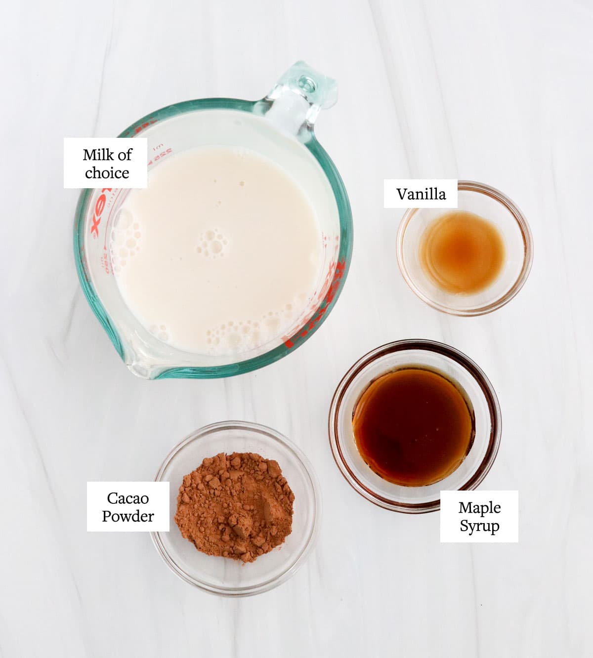healthy hot chocolate ingredients in glass bowls on white surface.
