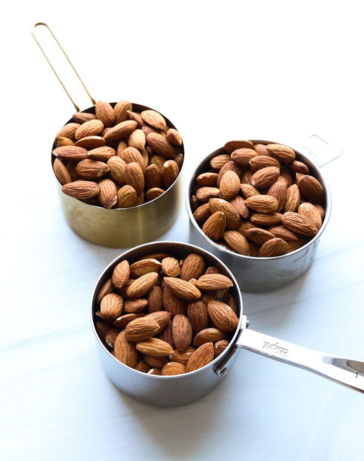 3 cups of almonds on a white surface.