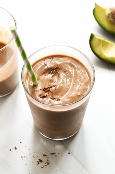 chocolate avocado smoothie with green straw and chocolate on top.