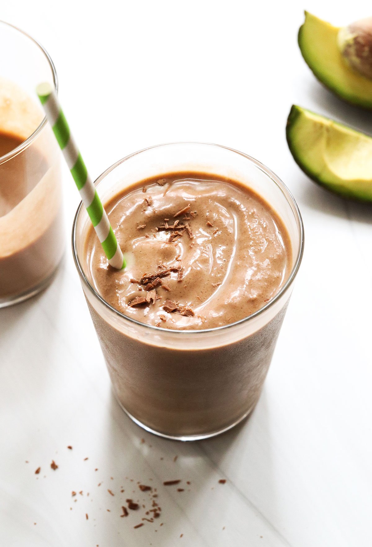 chocolate avocado smoothie with green straw and chocolate on top.